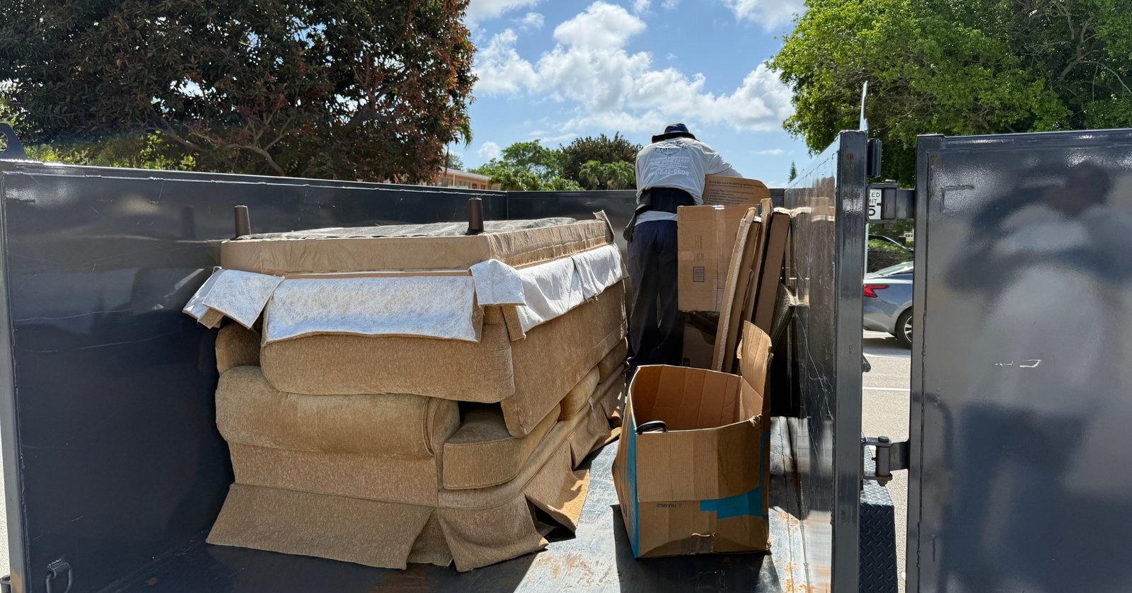 High Caliber Junk Removal team member loading couch and boxes into dump trailer during residential junk removal job in Broward County Florida